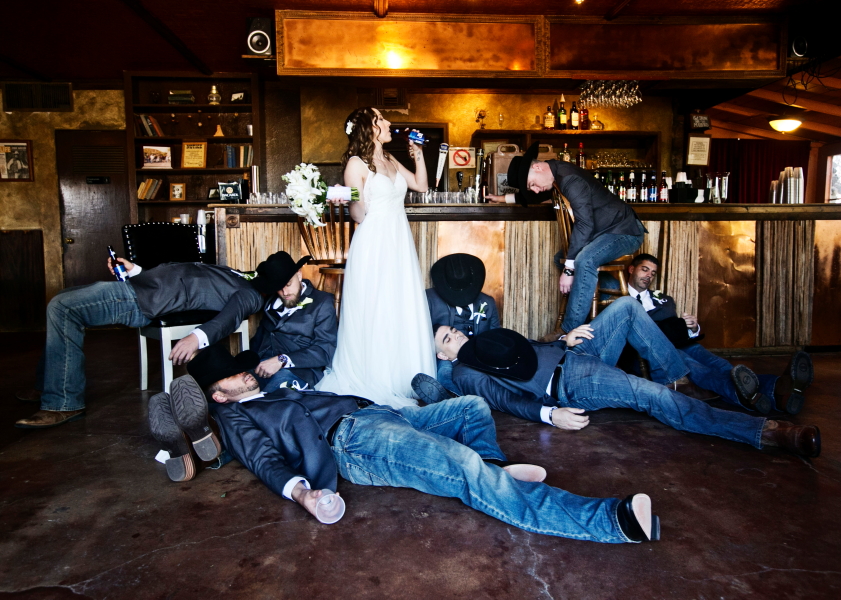 Bride is drinking and the groomsmen are pretending to be passed out in the bar